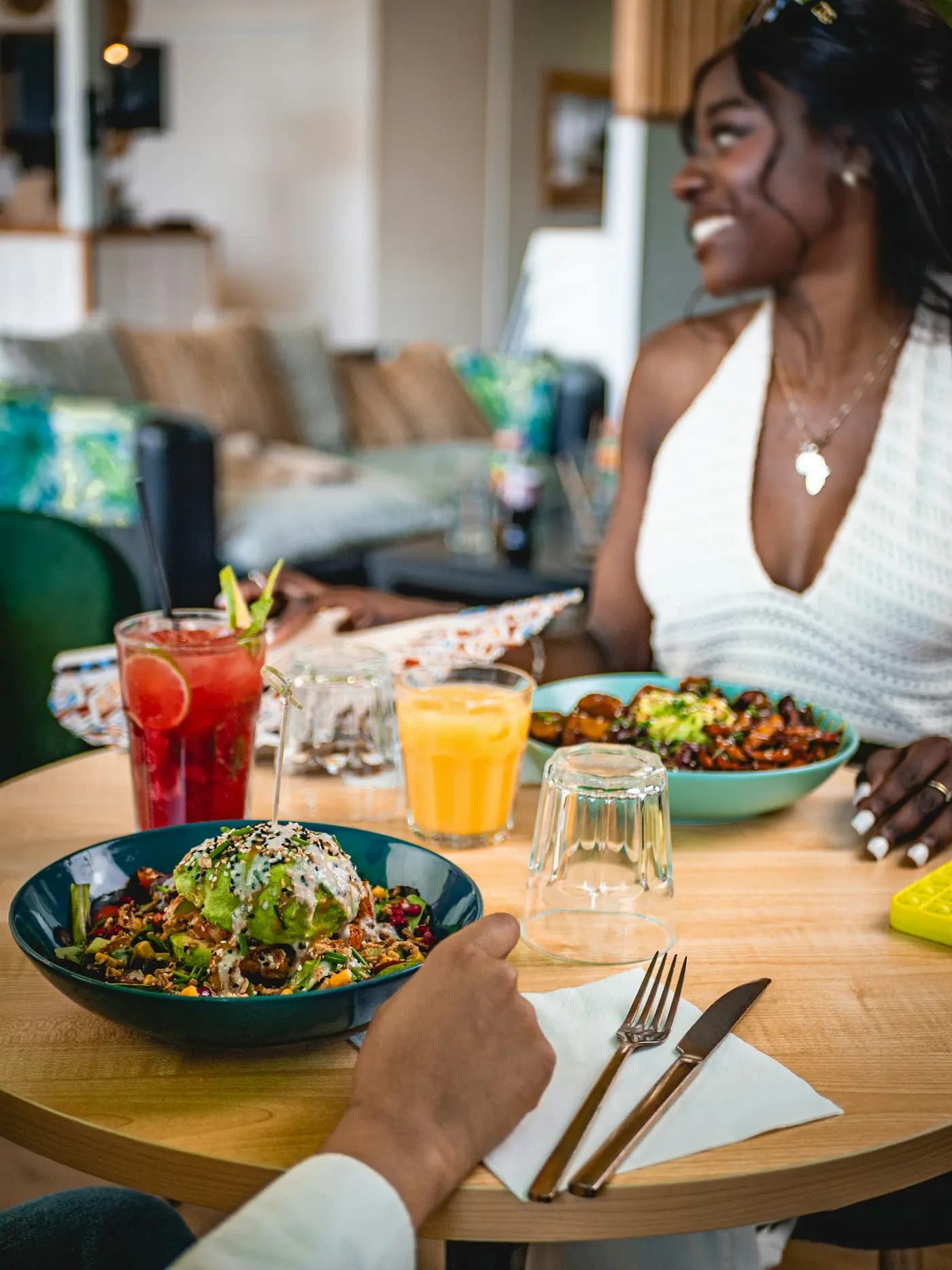 Une cliente sourit, attablée devant son assiette et un jus frais