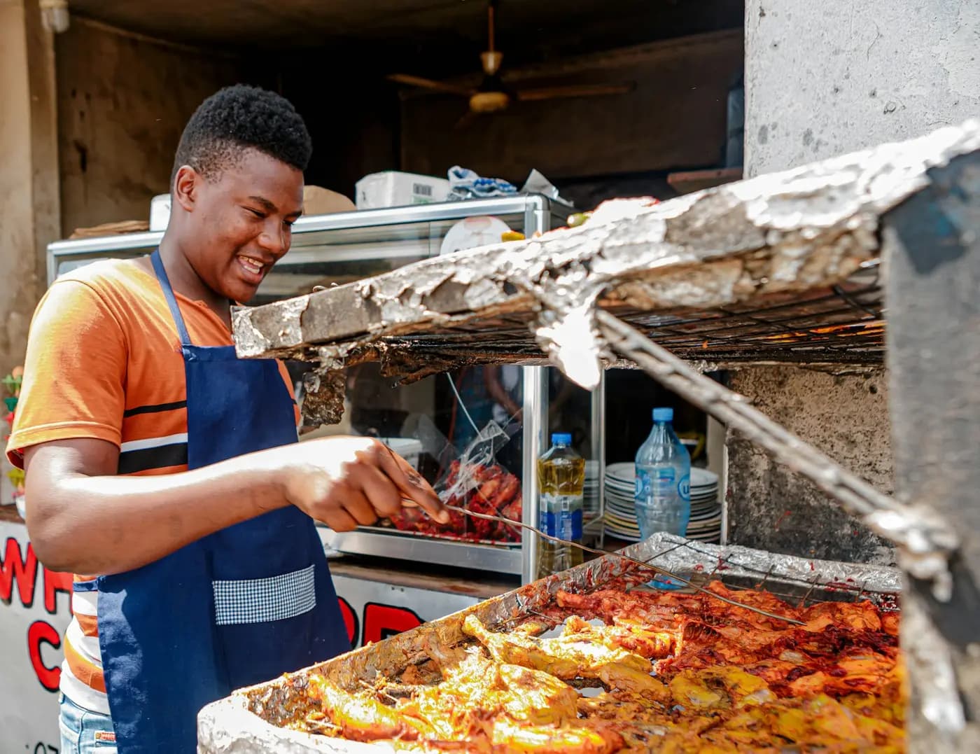 Un grilleur surveille ses poissons sur la braise, sous l’auvent de son stand